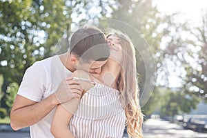 Handsome brunette guy, wearing white t-shirt, hugging and kissing pretty blond woman in stripy overall. Young couple in love,
