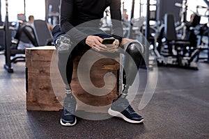 handsome brunette sportsman with bionic leg using smart phone at gym
