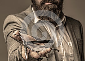 Handsome brutal man barber with beard and moustache hold barbershop retro razor blade and scissors, hair salon. Barber