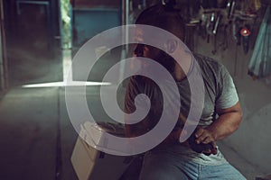 Handsome brutal man with a beard sitting on a motorcycle in his garage, wiping his hands and looking to the side