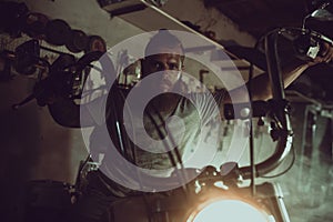 Handsome brutal man with a beard sitting on a motorcycle in his garage, wiping his hands and looking to the side