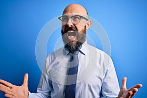 Handsome business bald man with beard wearing elegant tie and glasses over blue background crazy and mad shouting and yelling with