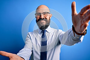 Handsome business bald man with beard wearing elegant tie and glasses over blue background looking at the camera smiling with open