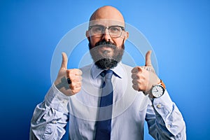 Handsome business bald man with beard wearing elegant tie and glasses over blue background success sign doing positive gesture