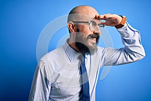 Handsome business bald man with beard wearing elegant tie and glasses over blue background very happy and smiling looking far away