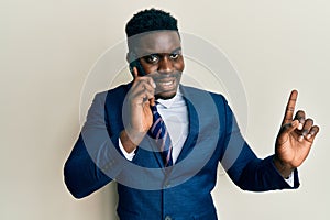 Handsome business black man having conversation talking on the smartphone smiling happy pointing with hand and finger to the side