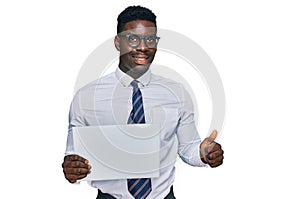Handsome business black man holding blank empty banner smiling happy and positive, thumb up doing excellent and approval sign