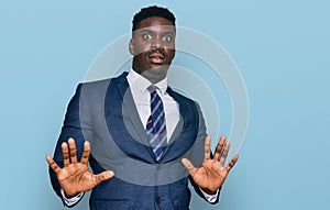 Handsome business black man wearing business suit and tie afraid and terrified with fear expression stop gesture with hands,