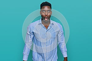 Handsome business black man wearing casual striped t shirt scared and amazed with open mouth for surprise, disbelief face