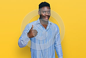 Handsome business black man wearing casual striped t shirt smiling happy and positive, thumb up doing excellent and approval sign