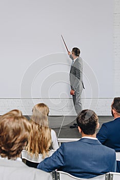 handsome business coach pointing on board with pointer stick during training