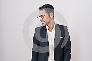 Handsome business hispanic man standing over white background looking away to side with smile on face, natural expression