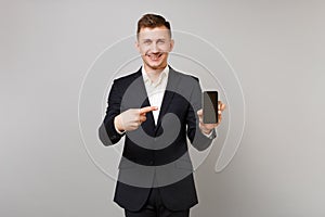Handsome business man in classic black suit pointing index finger on mobile phone with blank empty screen isolated on
