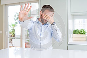 Handsome business man covering eyes with hands and doing stop gesture with sad and fear expression