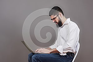 Handsome business man in glasses and suit holding laptop in hands and writing something. Side view. Isolated gray