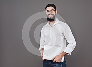 Handsome business man in glasses and suit holding laptop in hands and writing something. Side view. Isolated gray