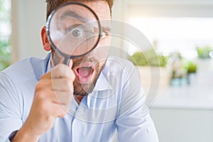 Handsome business man holding magnifying glass close to face, big eyes and funny expression