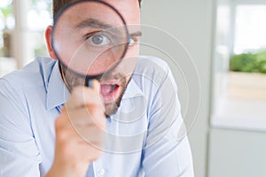 Handsome business man holding magnifying glass close to face, big eyes and funny expression
