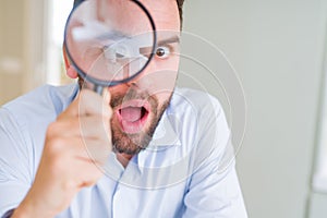 Handsome business man holding magnifying glass close to face, big eyes and funny expression
