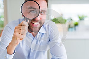 Handsome business man holding magnifying glass close to face, big eyes and funny expression