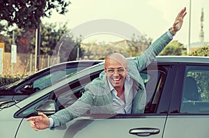 Handsome business man looking out of his new car window hands raised. Success, happiness, travel concept