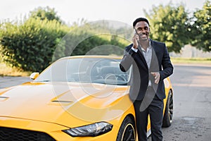 Handsome business man standing outdoors near his luxury yellow auto.