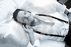 Handsome business man with suspenders lying on hotel room bed smiling while listening to music on headphones