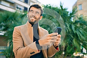 Handsome business man wearing elegant jacket using smartphone smiling happy outdoors