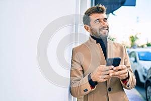 Handsome business man wearing elegant jacket using smartphone smiling happy outdoors