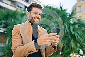 Handsome business man wearing elegant jacket using smartphone smiling happy outdoors