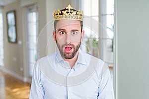 Handsome business man wearing golden crown as a king or prince afraid and shocked with surprise expression, fear and excited face