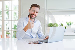 Handsome business man working using computer laptop happy with big smile doing ok sign, thumb up with fingers, excellent sign