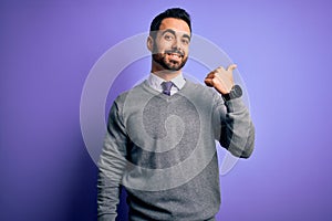 Handsome businessman with beard wearing casual tie standing over purple background smiling with happy face looking and pointing to