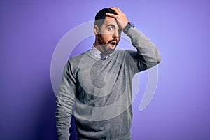 Handsome businessman with beard wearing casual tie standing over purple background surprised with hand on head for mistake,