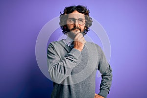 Handsome businessman with beard wearing tie and glasses standing over purple background with hand on chin thinking about question,