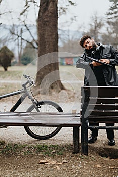 Handsome businessman with bicycle working on tablet in urban park