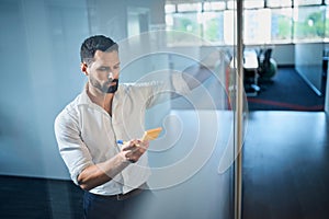 Handsome businessman brainstorming business ideas with notes on glass wall