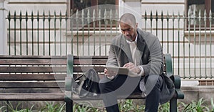 Handsome businessman browsing a tablet outside on a park bench. Serious male scrolling on a social media app while