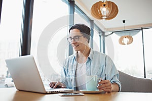 Handsome businessman in casual wear and eyeglasses is using a laptop in cafe