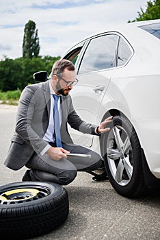 handsome businessman changing tires on car