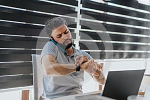 Handsome businessman checking time on wristwatch while having phone call.