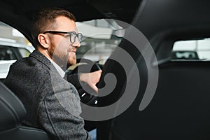 Handsome businessman driving car to airport, going on business side view, copy space. Happy man in stylish suit going to