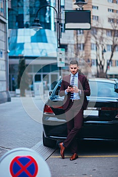 Handsome businessman entrepreneur standing proudly next to his parked limo at the middle of the business center