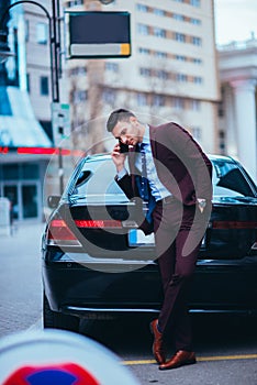 Handsome businessman entrepreneur standing proudly next to his parked limo at the middle of the business center