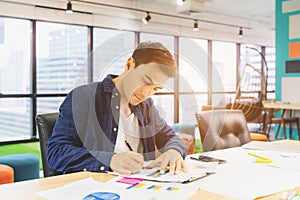 Handsome businessman in eyeglasses is making notes and smiling while working with a laptop at home