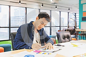 Handsome businessman in eyeglasses is making notes and smiling while working with a laptop at home