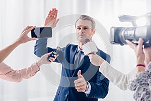 Handsome businessman giving interview to journalists in office, waving hand and