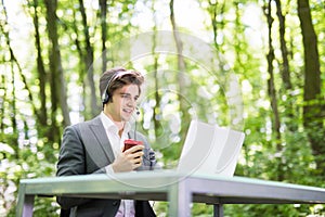 Handsome Businessman with headset sitting at the office desk with laptop computer and cup of coffee in hands in call center in gre