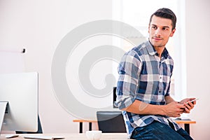 Handsome businessman holding smartphone and looking away