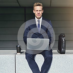 Handsome businessman with laptop looking at camera